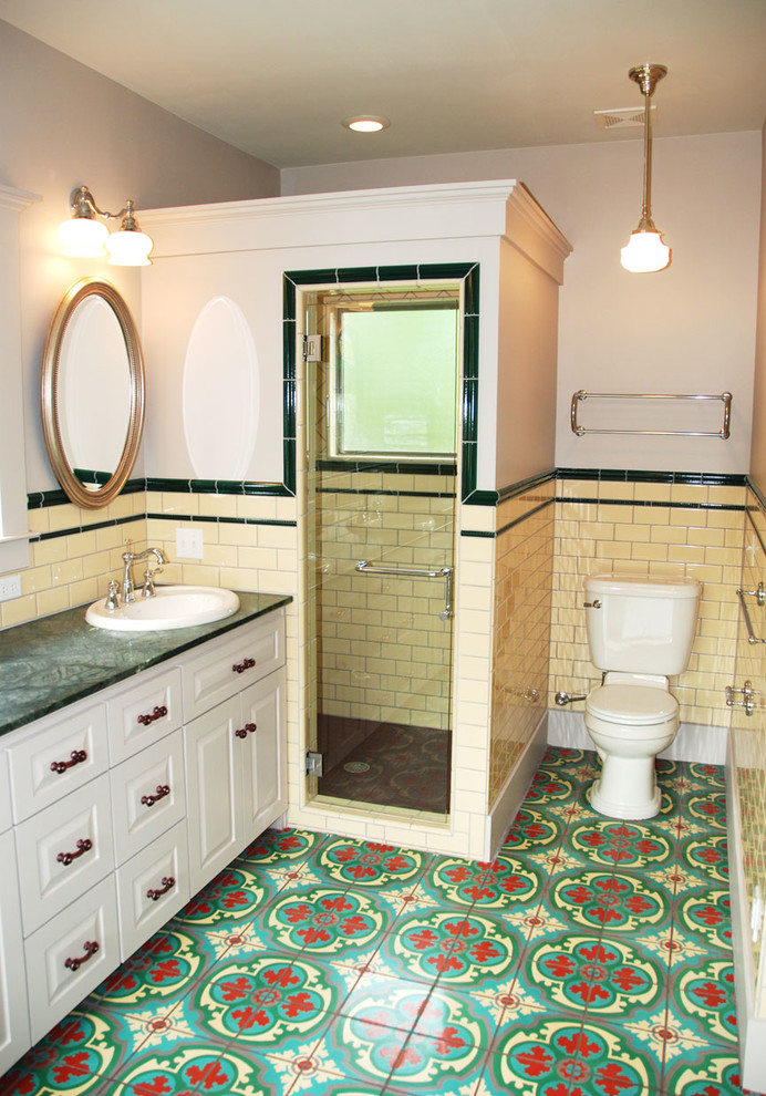 Design ideas for a mid-sized mediterranean master bathroom in Denver with raised-panel cabinets, white cabinets, a corner shower, a two-piece toilet, yellow tile, subway tile, beige walls, ceramic floors, a drop-in sink, multi-coloured floor, a hinged shower door and green benchtops.