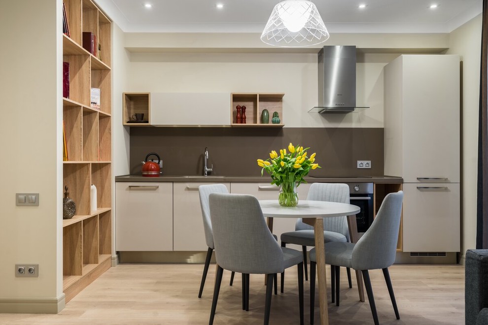 Contemporary single-wall open plan kitchen in Saint Petersburg with flat-panel cabinets, beige cabinets, brown splashback, stainless steel appliances, light hardwood floors, no island and beige floor.