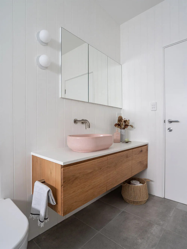 Modern inredning av ett stort vit vitt en-suite badrum, med möbel-liknande, skåp i mellenmörkt trä, ett fristående badkar, våtrum, en vägghängd toalettstol, vit kakel, skifferkakel, vita väggar, klinkergolv i porslin, ett fristående handfat, bänkskiva i akrylsten, grått golv och dusch med gångjärnsdörr