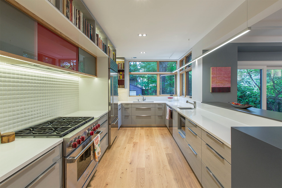 Photo of a mid-sized contemporary u-shaped kitchen in Toronto with an undermount sink, flat-panel cabinets, grey cabinets, quartz benchtops, white splashback, porcelain splashback, stainless steel appliances, light hardwood floors and a peninsula.