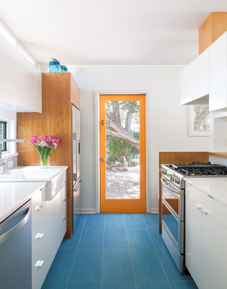 This is an example of a midcentury kitchen in Austin with a farmhouse sink, flat-panel cabinets, white cabinets, stainless steel appliances, no island, blue floor and white benchtop.
