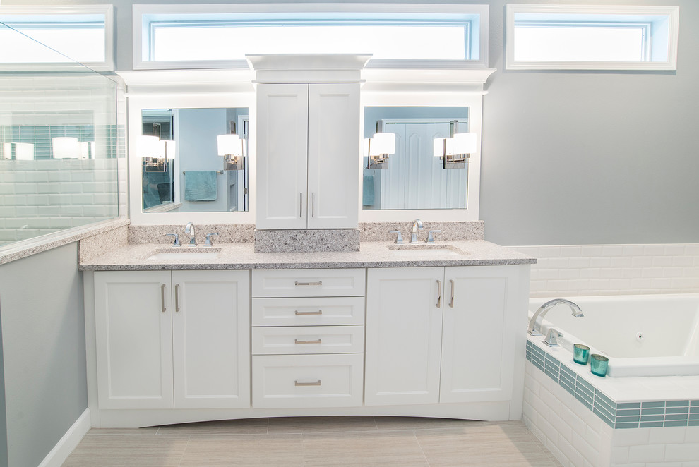 This is an example of a mid-sized transitional master bathroom in Orlando with shaker cabinets, white cabinets, a drop-in tub, a corner shower, white tile, subway tile, grey walls, laminate floors, an undermount sink, limestone benchtops, beige floor and a hinged shower door.