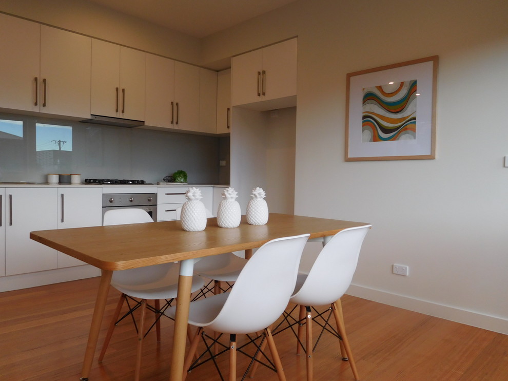 This is an example of a small contemporary single-wall open plan kitchen in Melbourne with flat-panel cabinets, white cabinets, grey splashback, glass sheet splashback, stainless steel appliances, medium hardwood floors and no island.