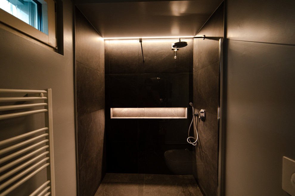 Idéer för små industriella brunt toaletter, med släta luckor, grå skåp, en toalettstol med hel cisternkåpa, svart kakel, porslinskakel, grå väggar, klinkergolv i porslin, ett fristående handfat, träbänkskiva och svart golv