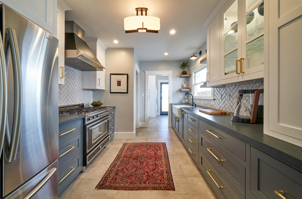 Photo of a mid-sized transitional galley kitchen in San Diego with a farmhouse sink, shaker cabinets, blue cabinets, quartz benchtops, white splashback, ceramic splashback, black appliances, porcelain floors, grey floor and grey benchtop.