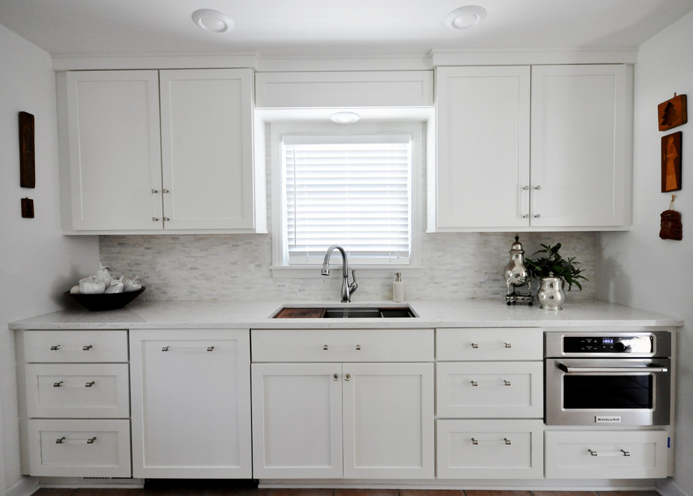 Design ideas for a transitional galley kitchen in Grand Rapids with a double-bowl sink, shaker cabinets, white cabinets, quartz benchtops, marble splashback and stainless steel appliances.