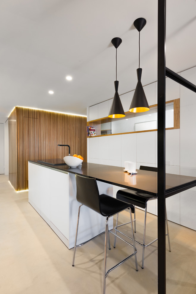 Design ideas for a mid-sized contemporary kitchen in Madrid with flat-panel cabinets, white cabinets, quartz benchtops, concrete floors, with island, black benchtop and beige floor.