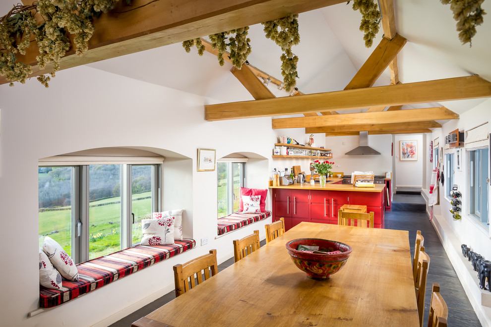 This is an example of a mid-sized country l-shaped eat-in kitchen in Gloucestershire with red cabinets, wood benchtops, slate floors and no island.