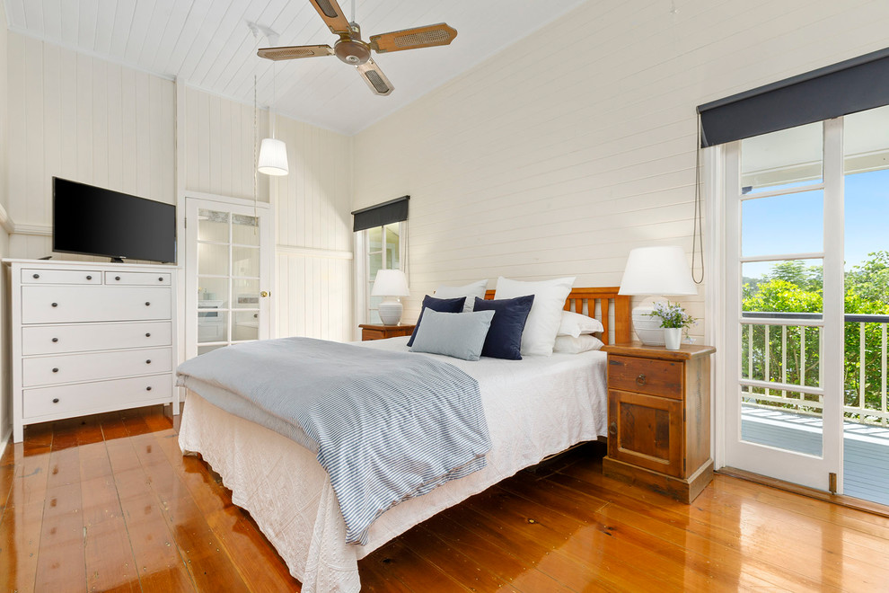 Country bedroom in Brisbane with white walls, medium hardwood floors and brown floor.