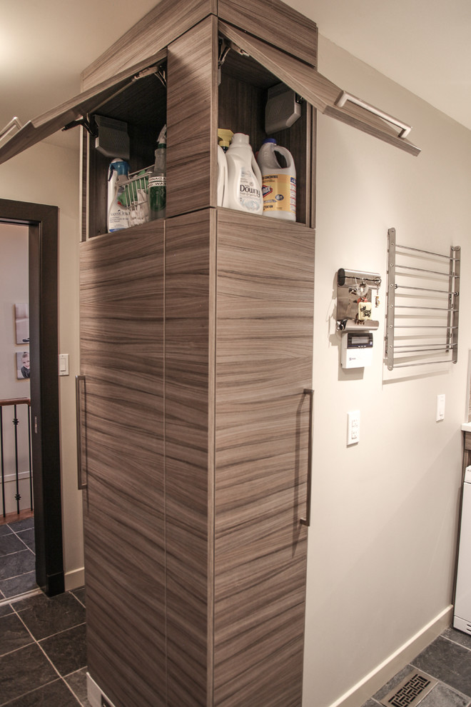 Photo of a mid-sized transitional l-shaped utility room in Calgary with an utility sink, flat-panel cabinets, grey cabinets, quartz benchtops, beige walls, slate floors and a side-by-side washer and dryer.