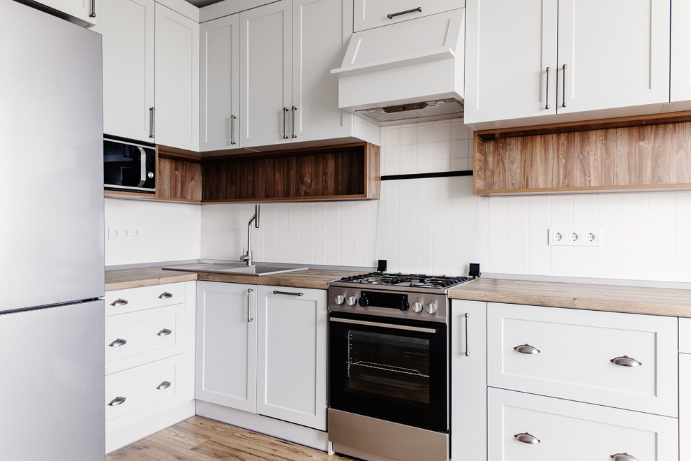 Eat-in kitchen - mid-sized transitional u-shaped dark wood floor and brown floor eat-in kitchen idea in DC Metro with a drop-in sink, recessed-panel cabinets, white cabinets, wood countertops, white backsplash, ceramic backsplash, stainless steel appliances, a peninsula and brown countertops