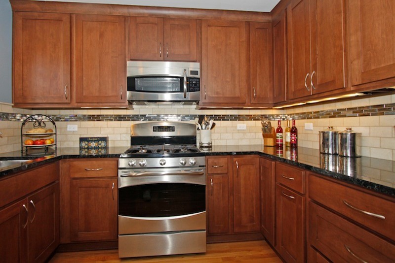 Mid-sized transitional u-shaped light wood floor eat-in kitchen photo in Chicago with an undermount sink, recessed-panel cabinets, medium tone wood cabinets, granite countertops, beige backsplash, stone tile backsplash, stainless steel appliances and no island