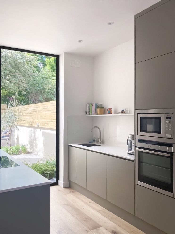 This is an example of a mid-sized scandinavian eat-in kitchen in Dublin with an integrated sink, flat-panel cabinets, grey cabinets, quartz benchtops, white splashback, engineered quartz splashback, panelled appliances, light hardwood floors, with island, brown floor and white benchtop.
