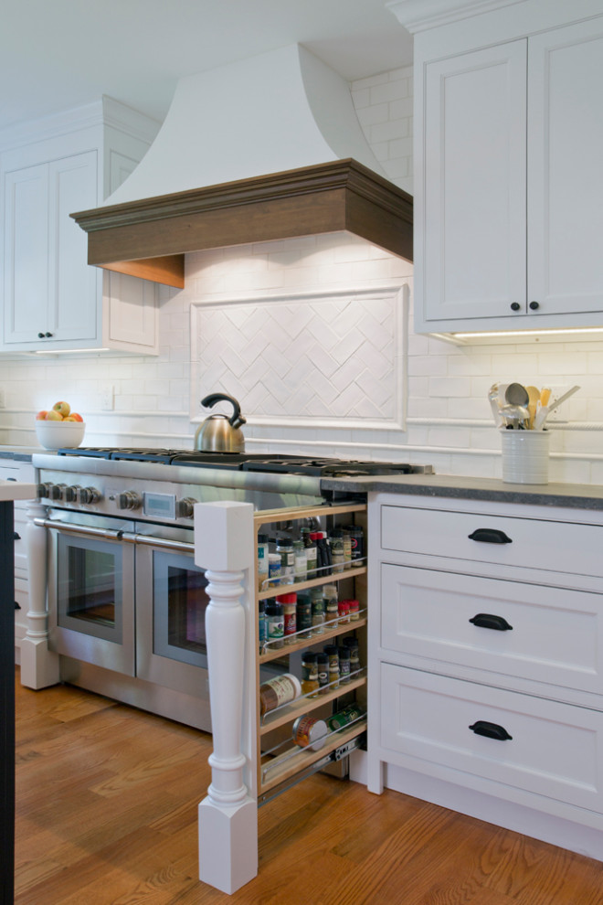 This is an example of a mid-sized transitional l-shaped eat-in kitchen in Other with a farmhouse sink, beaded inset cabinets, white cabinets, soapstone benchtops, white splashback, panelled appliances, light hardwood floors, with island, brown floor, black benchtop and timber.