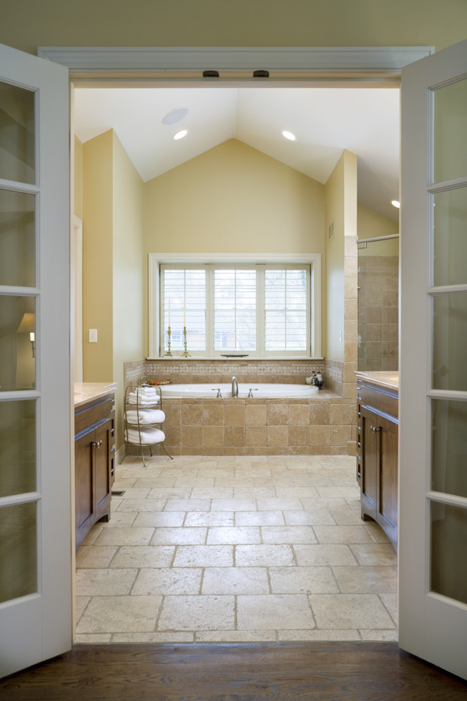 Expansive traditional master bathroom in Kansas City with an undermount sink, furniture-like cabinets, medium wood cabinets, granite benchtops, a freestanding tub, an alcove shower, brown tile, stone tile, yellow walls and limestone floors.