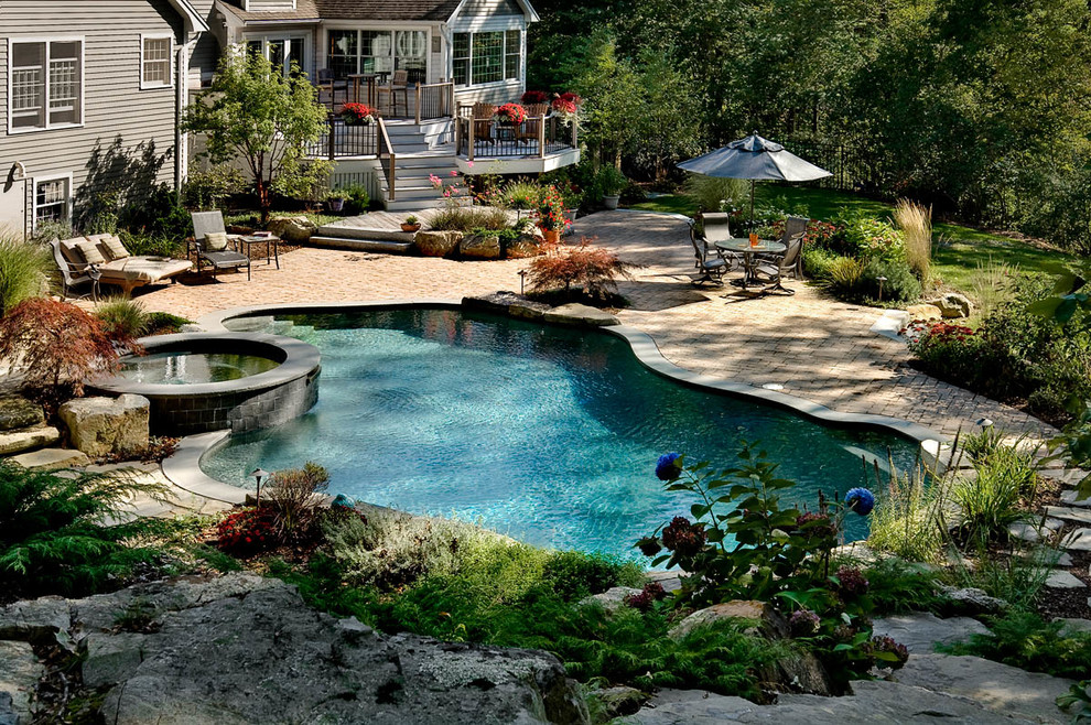 This is an example of a mid-sized traditional backyard custom-shaped natural pool in Boston with concrete pavers and a hot tub.