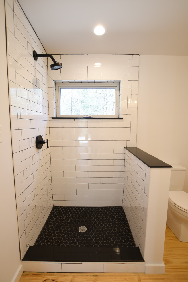 Photo of a mid-sized midcentury kids bathroom in New York with flat-panel cabinets, an alcove shower, a one-piece toilet, white walls, an open shower, a single vanity, a freestanding vanity, black cabinets, light hardwood floors, an integrated sink, solid surface benchtops, brown floor and white benchtops.