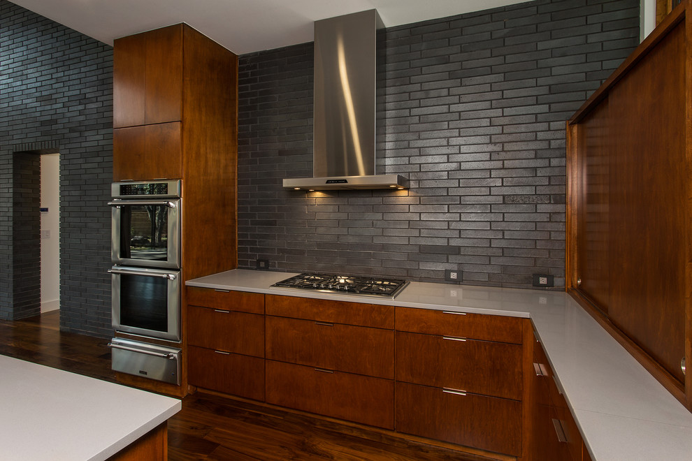 Photo of a mid-sized midcentury u-shaped open plan kitchen in Dallas with an undermount sink, flat-panel cabinets, medium wood cabinets, solid surface benchtops, white splashback, ceramic splashback, stainless steel appliances, dark hardwood floors, with island and brown floor.