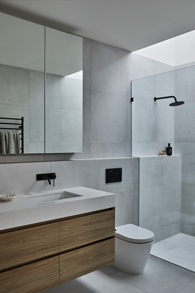 Photo of a small modern bathroom in Melbourne with light wood cabinets, a wall-mount toilet, gray tile, mosaic tile, grey walls, an undermount sink, engineered quartz benchtops, grey floor, grey benchtops and a floating vanity.