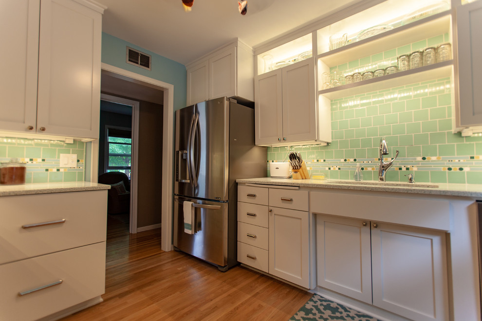 Photo of a midcentury separate kitchen in Minneapolis with an undermount sink, shaker cabinets, white cabinets, recycled glass benchtops, green splashback, mosaic tile splashback, stainless steel appliances, medium hardwood floors, no island, brown floor and white benchtop.