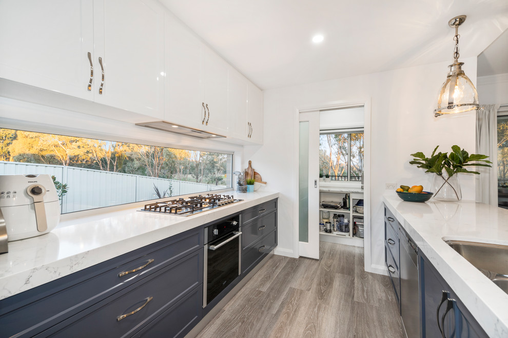 Mid-sized traditional galley kitchen pantry in Other with an undermount sink, shaker cabinets, blue cabinets, quartz benchtops, metallic splashback, window splashback, stainless steel appliances, linoleum floors, with island, grey floor and white benchtop.