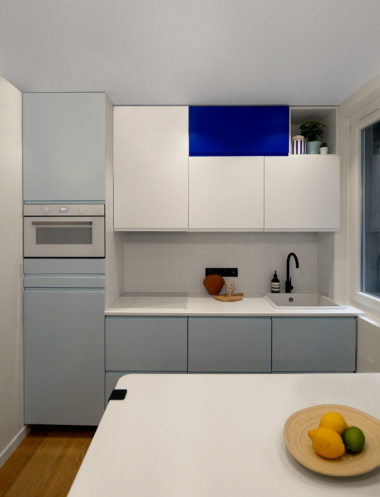 Inspiration for a small modern single-wall open plan kitchen in Paris with a single-bowl sink, beaded inset cabinets, blue cabinets, laminate benchtops, white splashback, ceramic splashback, white appliances, vinyl floors, beige floor and white benchtop.