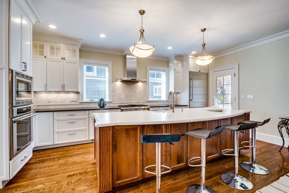 Inspiration for a mid-sized transitional l-shaped medium tone wood floor and brown floor open concept kitchen remodel in Boston with recessed-panel cabinets, white cabinets, an island, a farmhouse sink, soapstone countertops, beige backsplash, ceramic backsplash and stainless steel appliances
