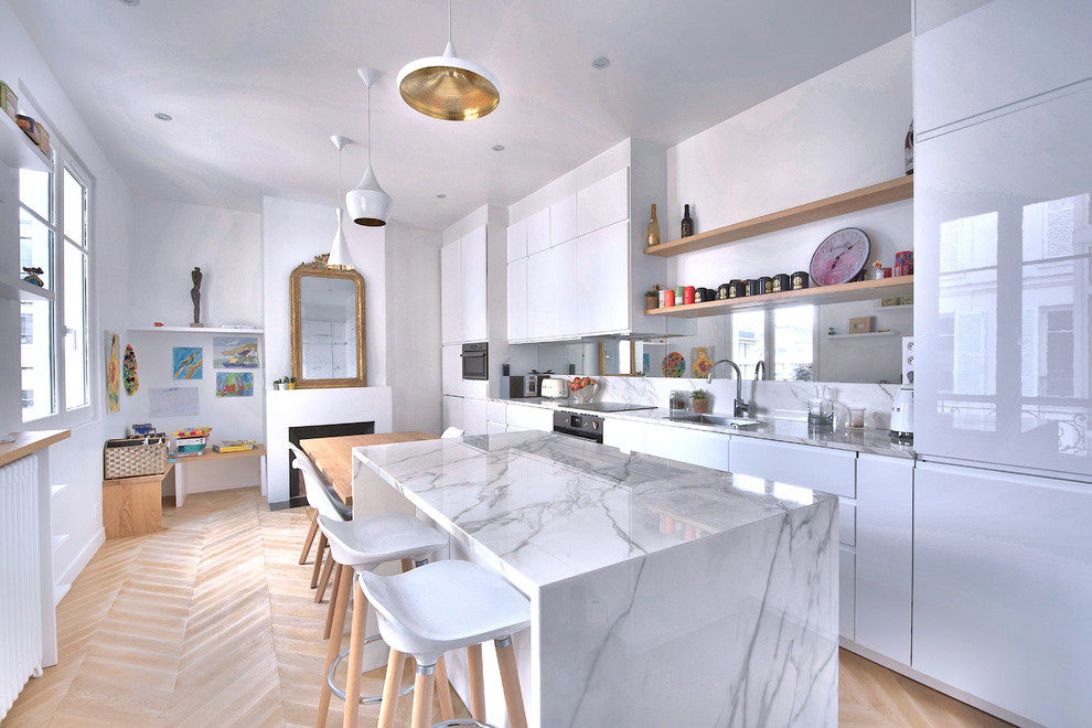 Contemporary galley eat-in kitchen in Paris with an undermount sink, flat-panel cabinets, white cabinets, white splashback, mirror splashback, stainless steel appliances, light hardwood floors, with island, beige floor, white benchtop and marble benchtops.