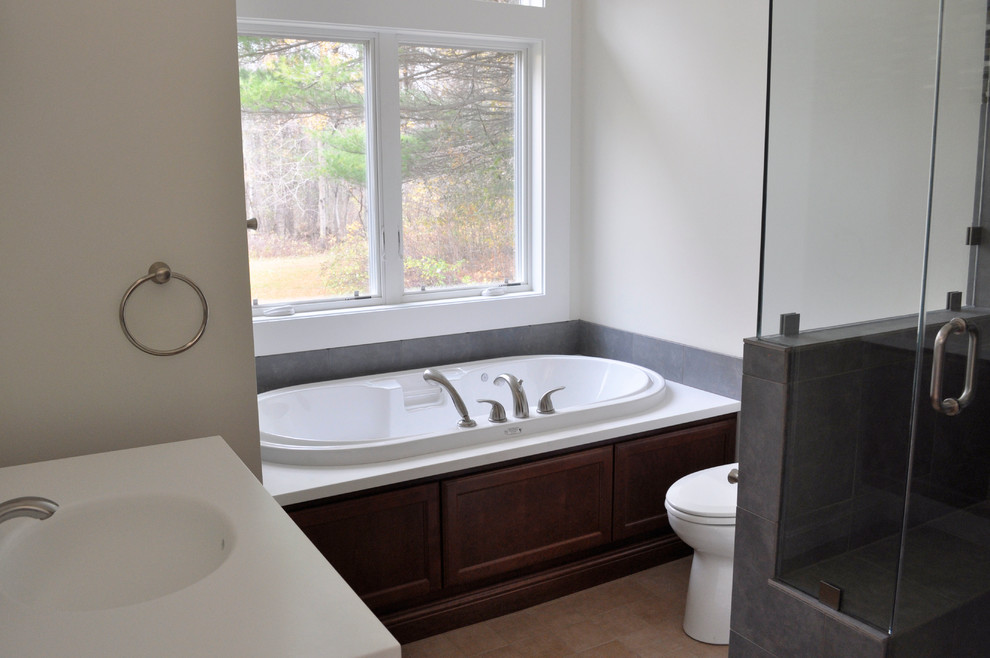 This is an example of a small contemporary master bathroom in Burlington with an integrated sink, shaker cabinets, dark wood cabinets, solid surface benchtops, an alcove tub, a corner shower, a two-piece toilet, gray tile, porcelain tile, white walls and porcelain floors.