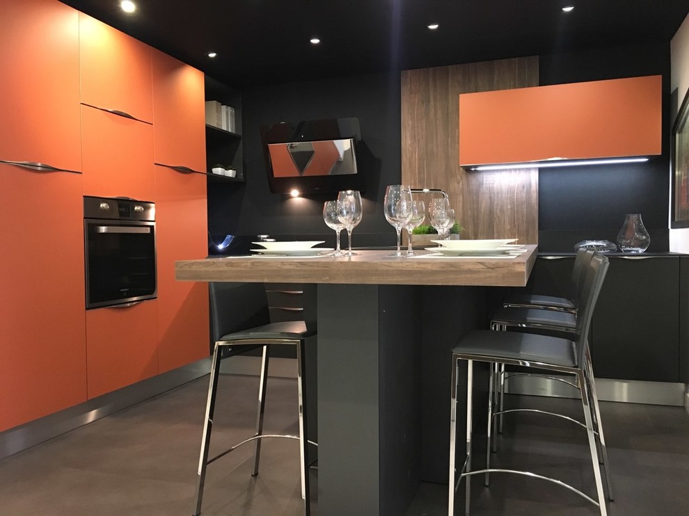 Mid-sized industrial open plan kitchen in Nice with an integrated sink, flat-panel cabinets, orange cabinets, laminate benchtops, black splashback, stainless steel appliances, ceramic floors, a peninsula and grey floor.