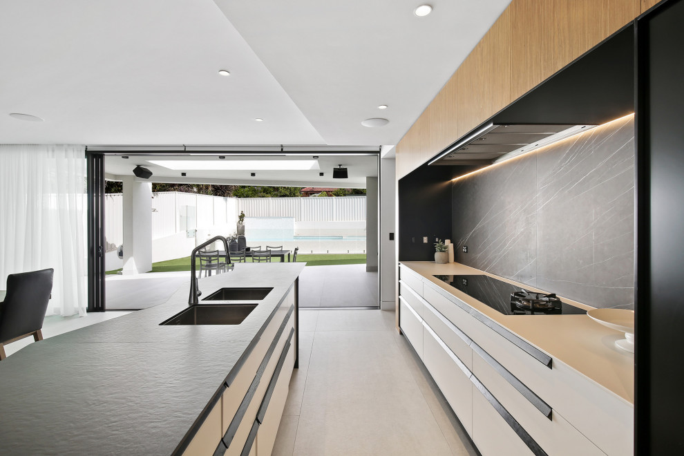 This is an example of a large contemporary galley eat-in kitchen in Sydney with a double-bowl sink, flat-panel cabinets, white cabinets, black splashback, porcelain splashback, stainless steel appliances, porcelain floors, with island, grey floor and white benchtop.