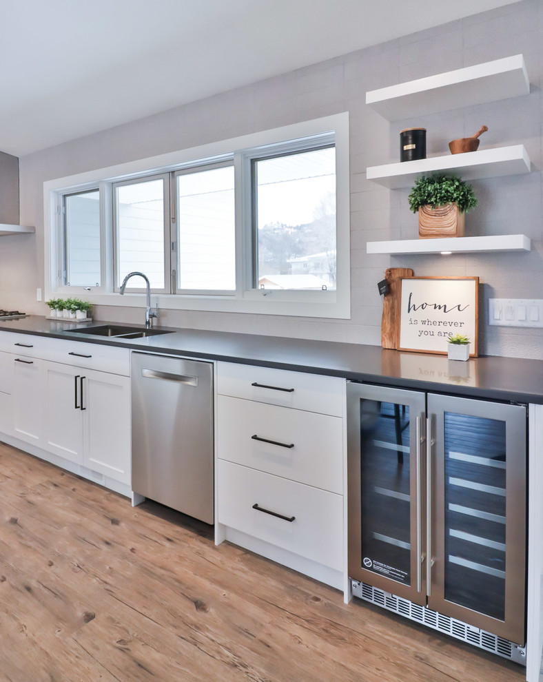 Example of a large transitional l-shaped vinyl floor and brown floor open concept kitchen design with an undermount sink, flat-panel cabinets, white cabinets, quartz countertops, gray backsplash, porcelain backsplash, stainless steel appliances and an island