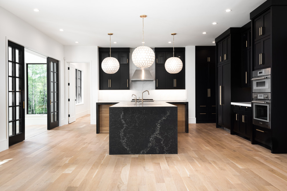 Kitchen - mid-sized transitional u-shaped light wood floor kitchen idea with an undermount sink, shaker cabinets, black cabinets, quartz countertops, white backsplash, quartz backsplash, stainless steel appliances, an island and black countertops