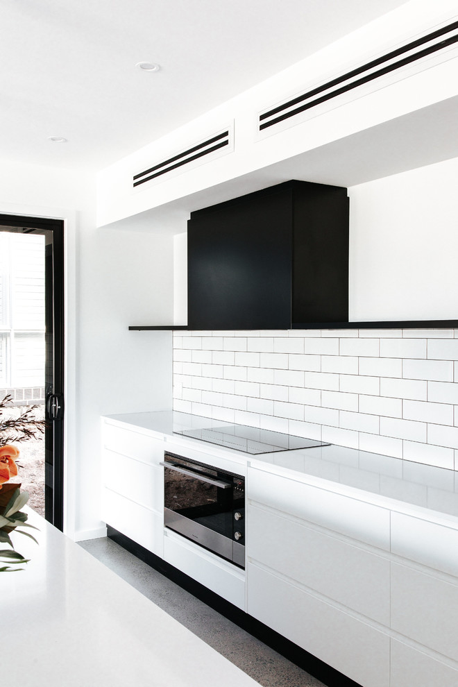 Design ideas for a mid-sized modern galley kitchen in Wollongong with a double-bowl sink, flat-panel cabinets, white cabinets, quartz benchtops, white splashback, ceramic splashback, stainless steel appliances, concrete floors, with island, grey floor and white benchtop.