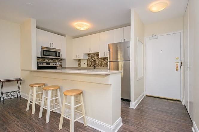 Mid-sized transitional single-wall medium tone wood floor and brown floor open concept kitchen photo in Chicago with white cabinets, multicolored backsplash, stainless steel appliances, a peninsula, a drop-in sink, flat-panel cabinets, granite countertops and glass tile backsplash