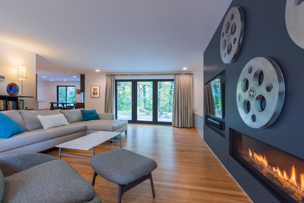 This is an example of a mid-sized contemporary open concept family room in Columbus with blue walls, medium hardwood floors, a ribbon fireplace, a plaster fireplace surround, a wall-mounted tv and brown floor.