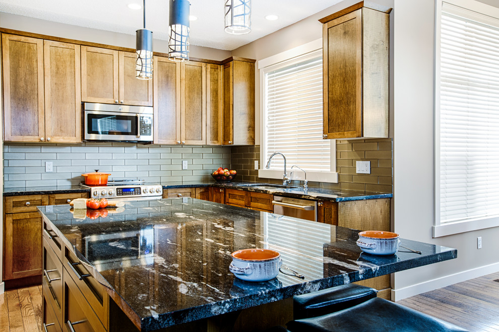 Mid-sized mountain style u-shaped medium tone wood floor and brown floor eat-in kitchen photo in Calgary with an undermount sink, shaker cabinets, medium tone wood cabinets, granite countertops, gray backsplash, glass tile backsplash, stainless steel appliances and an island
