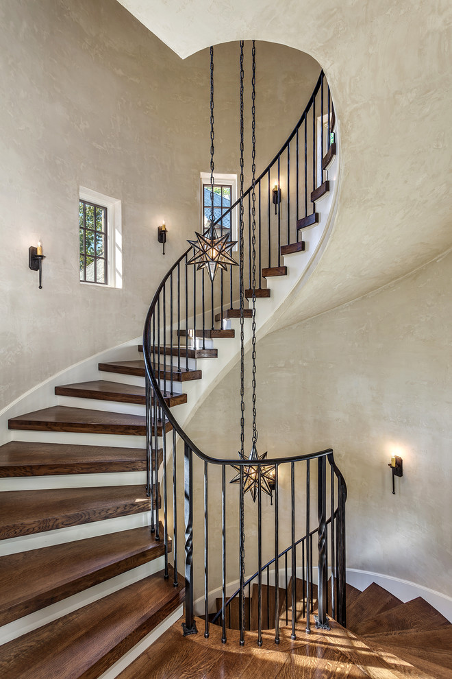 Photo of a large mediterranean wood spiral staircase in Other with painted wood risers and metal railing.
