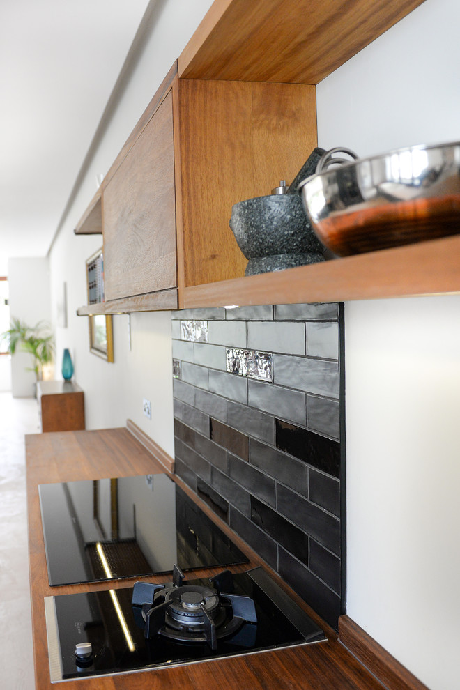 Mid-sized contemporary open plan kitchen in Sussex with flat-panel cabinets, blue cabinets, wood benchtops, black splashback, ceramic splashback, black appliances, concrete floors and with island.