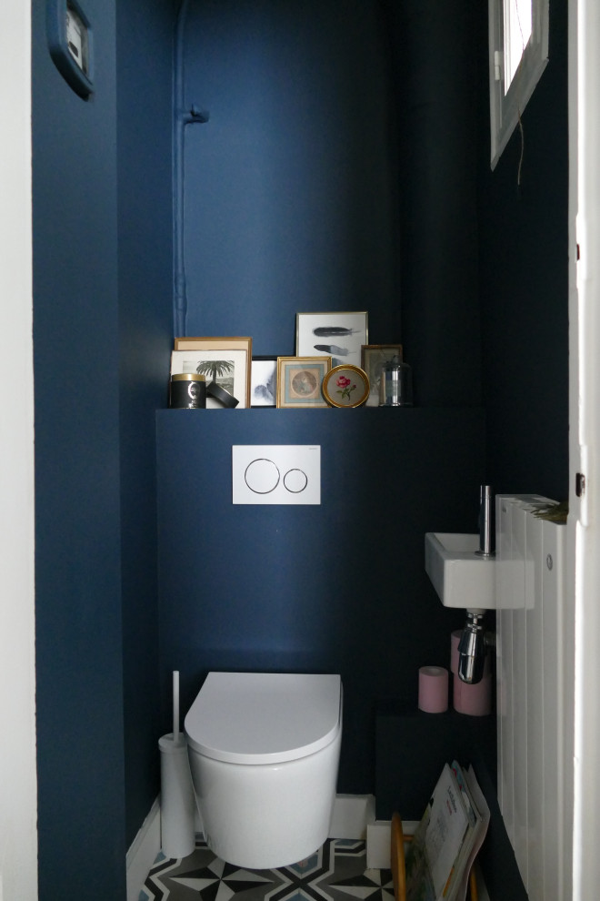 Modelo de aseo tradicional renovado pequeño con sanitario de pared, paredes azules, suelo de azulejos de cemento, lavabo suspendido y suelo gris