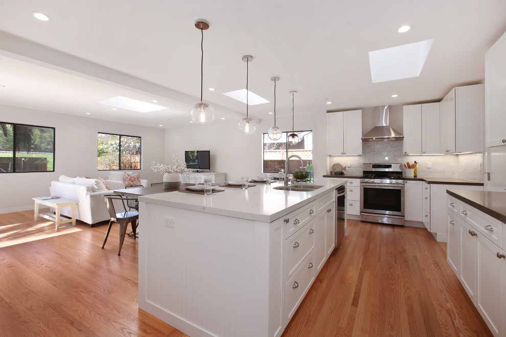 Design ideas for a large transitional l-shaped open plan kitchen in San Francisco with a double-bowl sink, shaker cabinets, white cabinets, quartzite benchtops, white splashback, stone tile splashback, stainless steel appliances, medium hardwood floors, with island and brown floor.