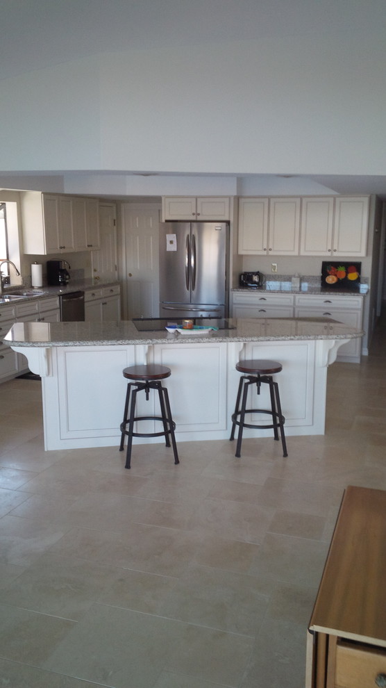 This is an example of a mid-sized contemporary l-shaped eat-in kitchen in Phoenix with a double-bowl sink, recessed-panel cabinets, white cabinets, granite benchtops, stainless steel appliances, limestone floors and with island.