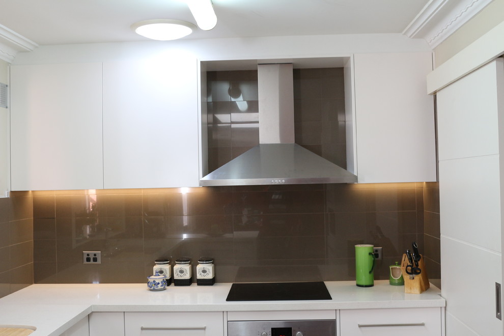 Photo of a large modern u-shaped open plan kitchen in Sydney with an undermount sink, flat-panel cabinets, white cabinets, quartz benchtops, brown splashback, glass sheet splashback, stainless steel appliances, multiple islands and white benchtop.