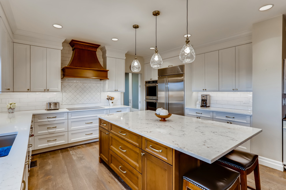 Design ideas for a traditional open plan kitchen in Denver with a submerged sink, shaker cabinets, brown cabinets, engineered stone countertops, white splashback, metro tiled splashback, stainless steel appliances, medium hardwood flooring, an island and brown floors.