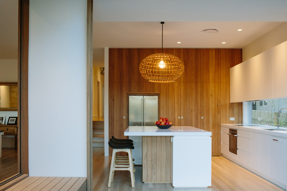 This is an example of a contemporary l-shaped kitchen in Sydney with flat-panel cabinets, white cabinets, stainless steel appliances, light hardwood floors and with island.