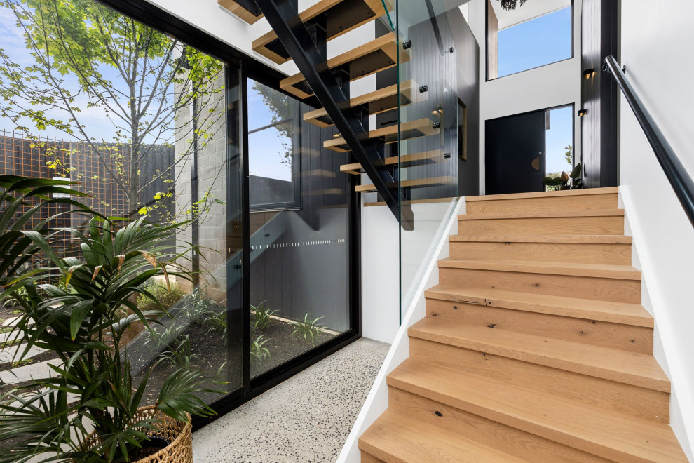 Пример оригинального дизайна: большая лестница в современном стиле с деревянными ступенями и стеклянными перилами