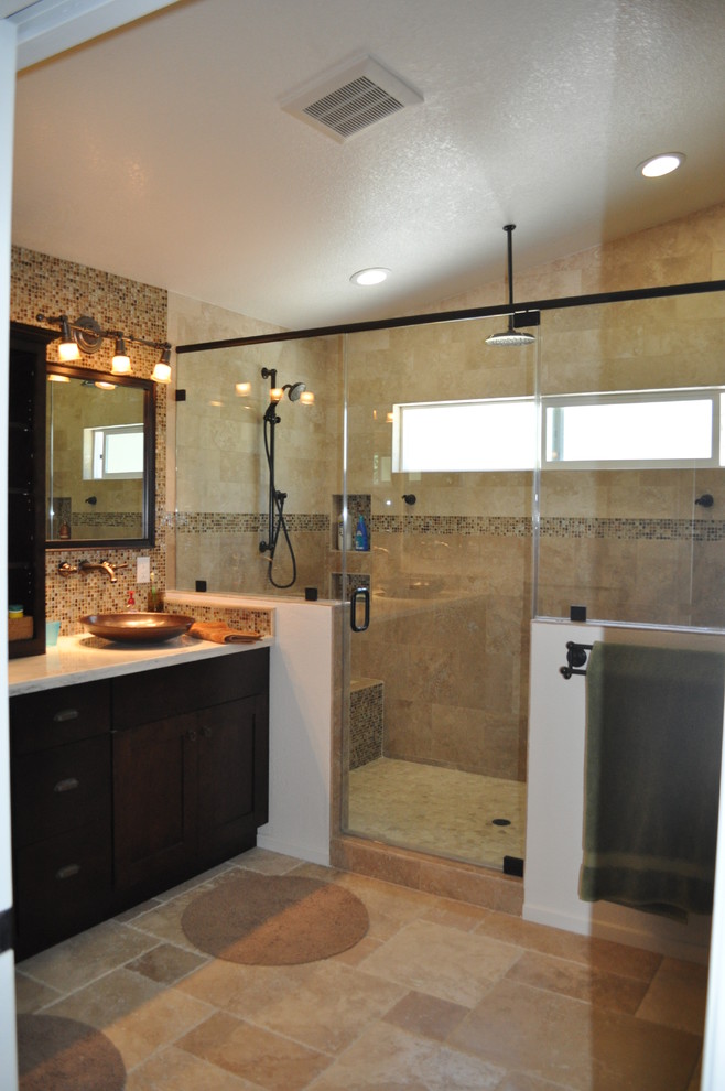 This is an example of a large contemporary master bathroom in Orange County with recessed-panel cabinets, dark wood cabinets, a double shower, beige tile, travertine, beige walls, travertine floors, a vessel sink, solid surface benchtops, beige floor and a hinged shower door.