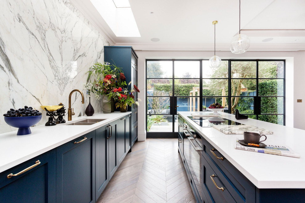 Large contemporary kitchen in London with shaker cabinets, blue cabinets, quartz worktops, white splashback, marble splashback, black appliances, an island, brown floors and white worktops.