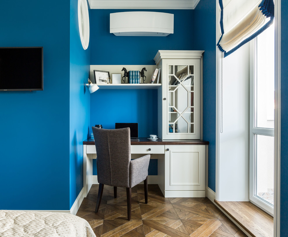 Стильный дизайн: кабинет в стиле неоклассика (современная классика) с синими стенами, темным паркетным полом и встроенным рабочим столом - последний тренд
