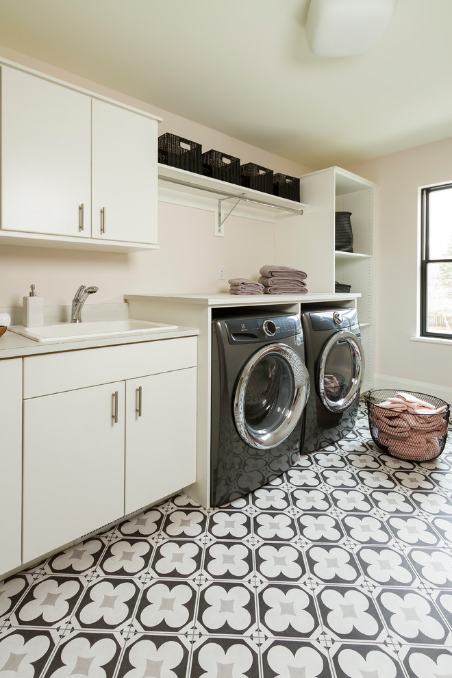 Inspiration for a large transitional single-wall dedicated laundry room in Minneapolis with a drop-in sink, flat-panel cabinets, white cabinets, laminate benchtops, pink walls, a side-by-side washer and dryer, multi-coloured floor, concrete floors and white benchtop.
